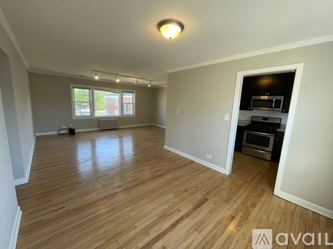A spacious room with wooden flooring and a kitchen area in the back.