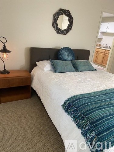 A bedroom with a bed, a nightstand with a lamp, and a mirror on the wall.