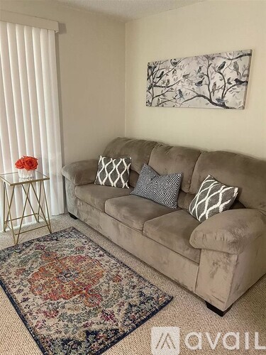 A living room with a beige couch, a floral rug, and a painting on the wall.