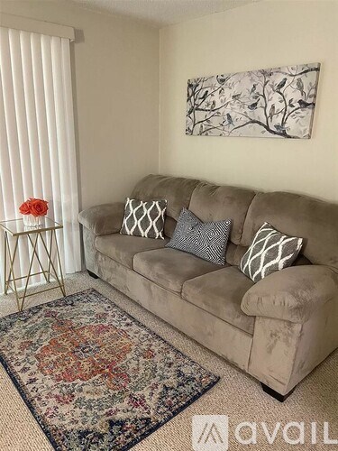 A living room with a beige couch, a floral rug, and a painting on the wall.
