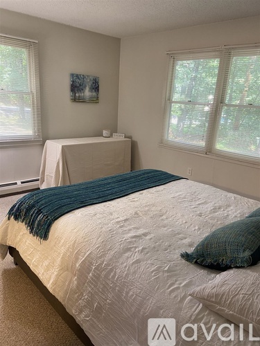 A bedroom with a bed covered in a white comforter and a blue throw.