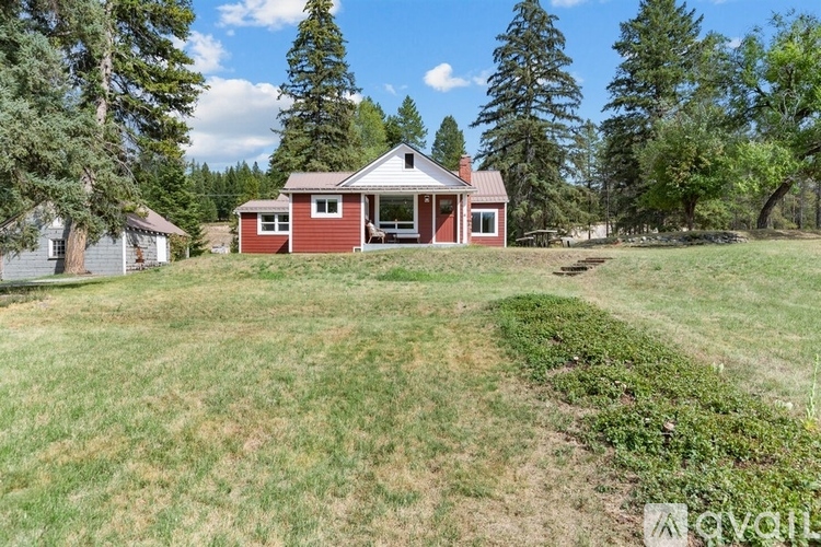 A red house with a white roof is surrounded by trees.