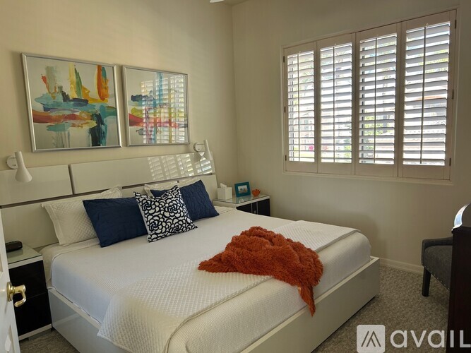 A bedroom with a white bed and a painting on the wall.