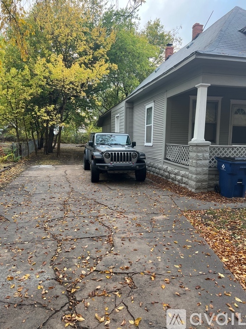 A black jeep is parked on a driveway with fallen leaves.