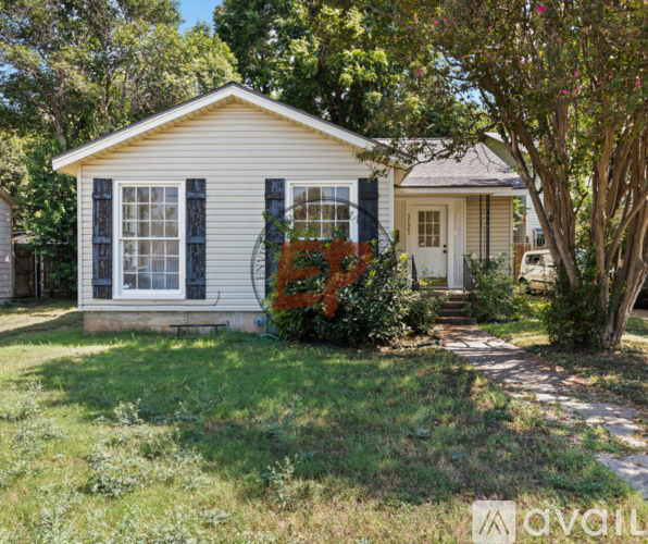A small white house with a porch and a tree in front.