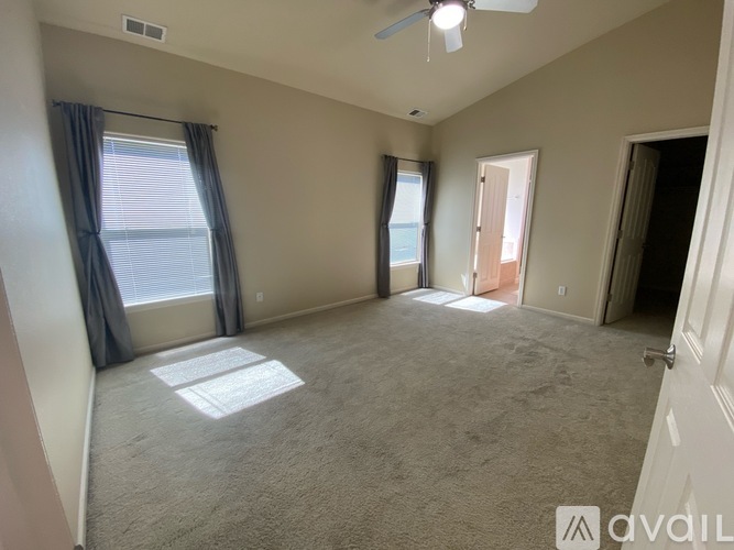 A spacious room with a carpeted floor, a ceiling fan, and a large window with curtains.