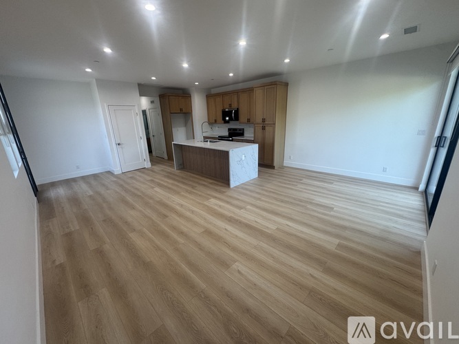 A spacious room with wooden flooring and a kitchen area.