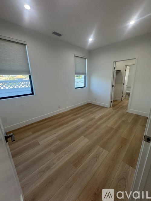 A room with wooden flooring and two windows.