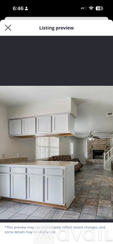 A living room with a fireplace and a kitchen area with white cabinets.
