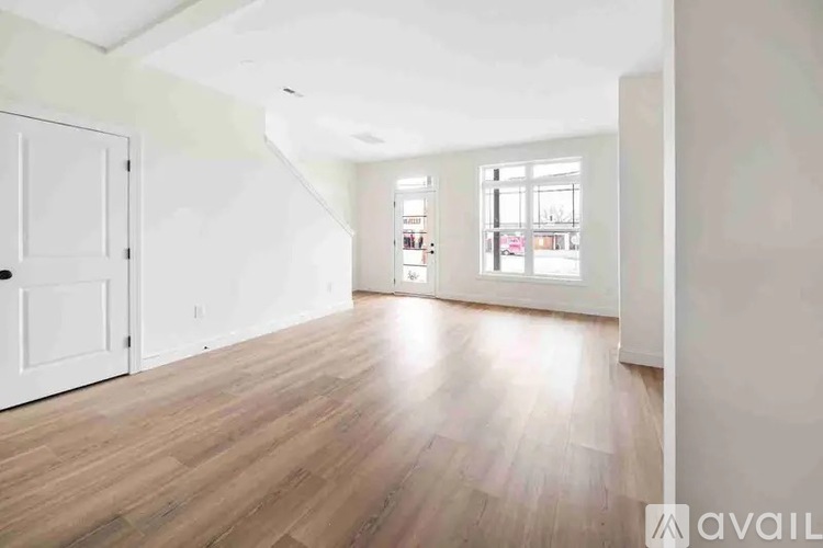 A room with wooden floors and white walls, with a door on the left and a window on the right.