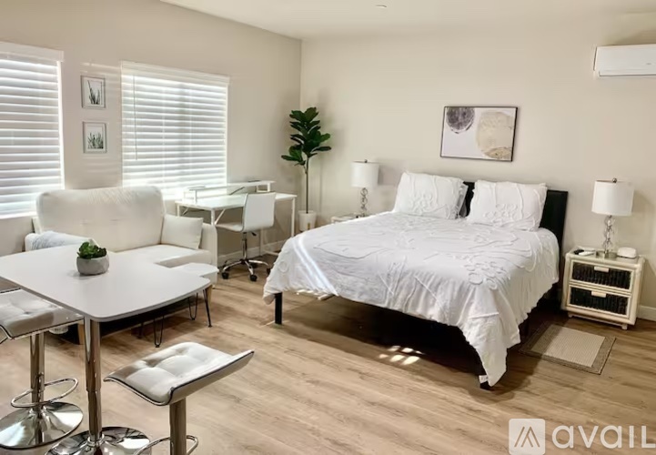 A bedroom with a bed, a desk with a chair, and a nightstand with a lamp.