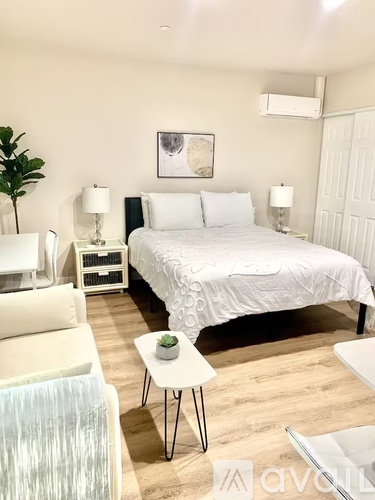 A bedroom with a large bed, a white chair, and a small table with a plant on it.