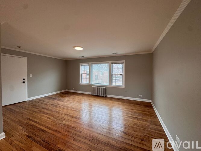 A spacious room with wooden floors and a window with a radiator beneath it.