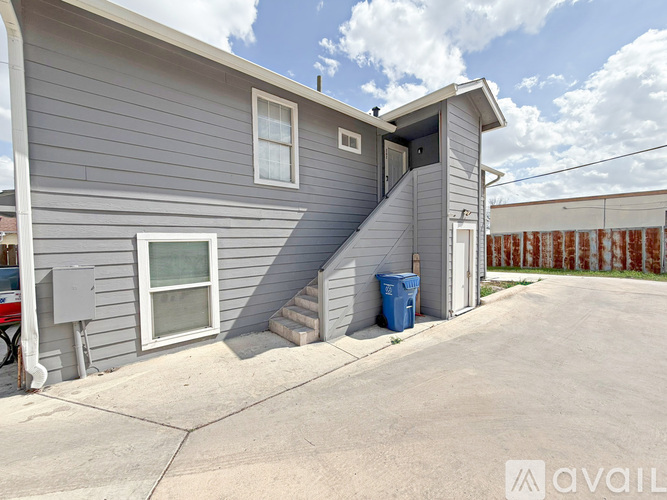 A grey house with a blue trash bin outside.