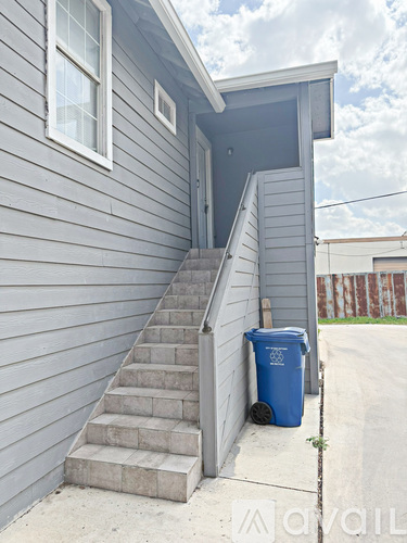 A blue trash can sits next to a concrete staircase outside a house.
