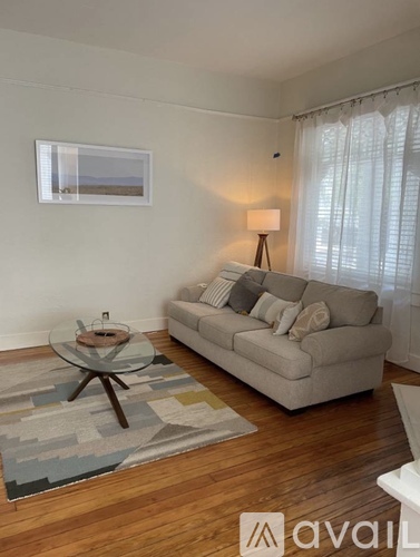 A living room with a couch, coffee table, and a window with curtains.