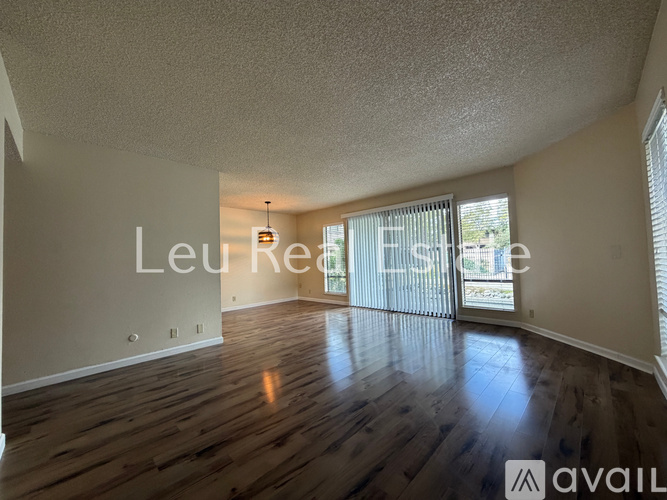A spacious room with wooden flooring and a large window with blinds.