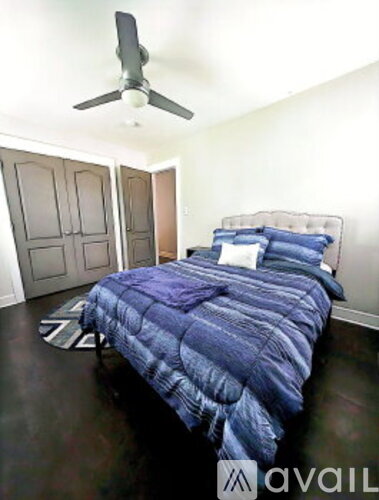A bedroom with a bed covered in a blue comforter and a ceiling fan above it.
