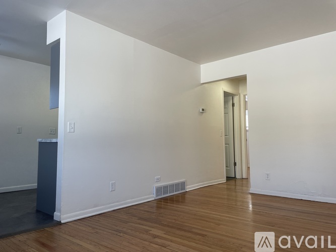 A room with wooden floors and white walls, with a doorway leading to another room.