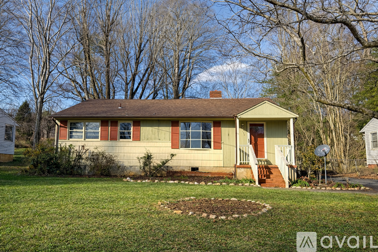 A house with a brown roof and a red door is surrounded by trees.