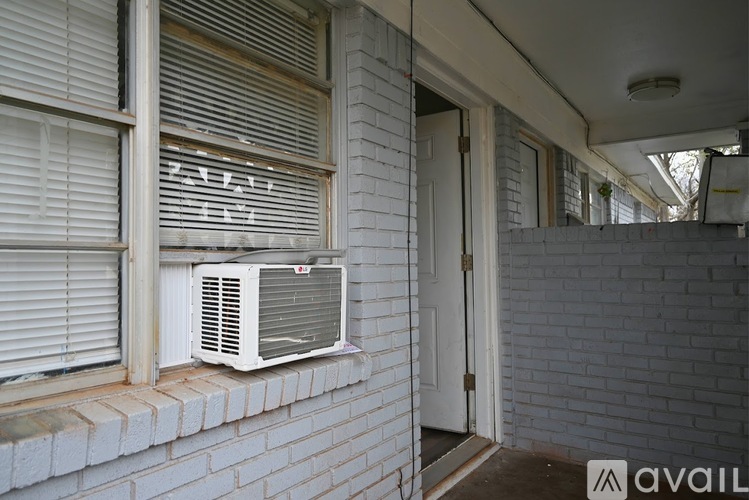 A white air conditioner is mounted on a brick wall outside a house.