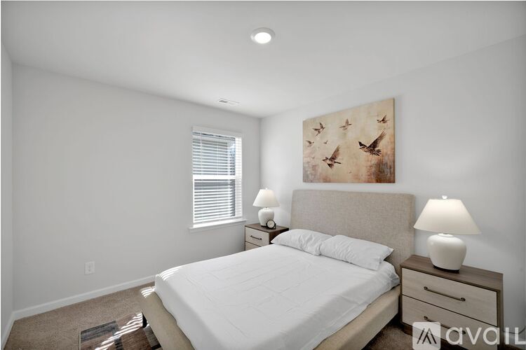 A bedroom with a large bed, two nightstands with lamps, and a painting on the wall.