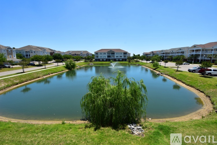 A lake in the middle of a grassy area with buildings in the background.
