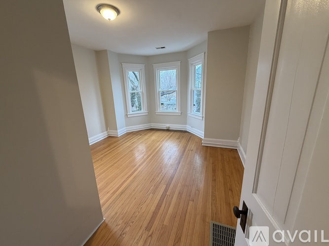 A room with wooden flooring and white walls, featuring a window with a view of trees outside.