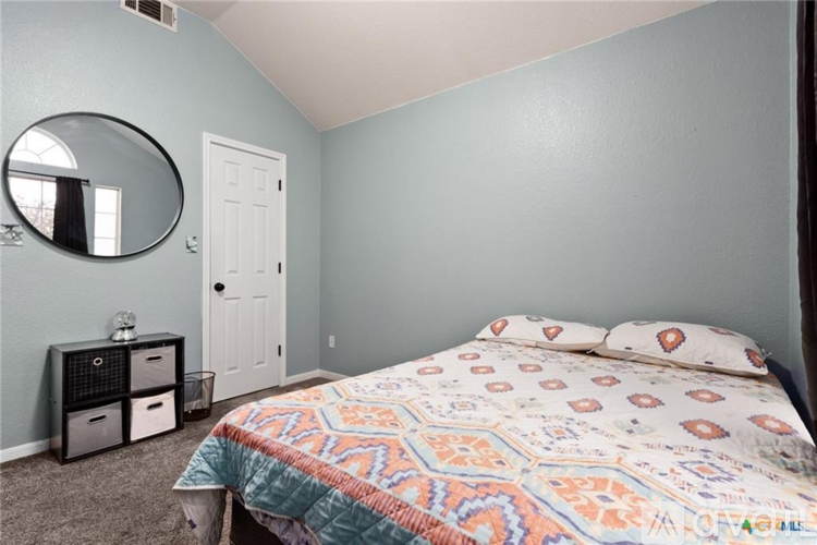 A bedroom with a bed, nightstand, and a round mirror on the wall.