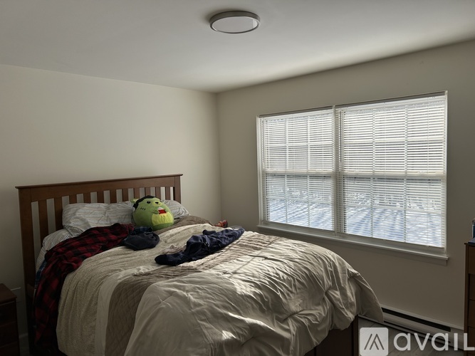 A bedroom with a bed, a teddy bear, and a window with blinds.