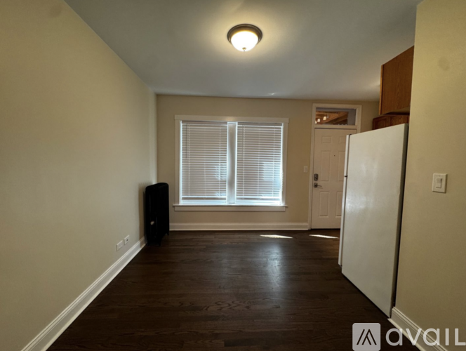 A room with a white door, a window with blinds, and a white refrigerator.