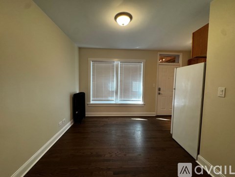 A room with a white door, a window with blinds, and a white refrigerator.