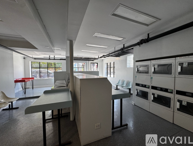 A kitchen area with a table and chairs in the foreground and a row of ovens in the background.