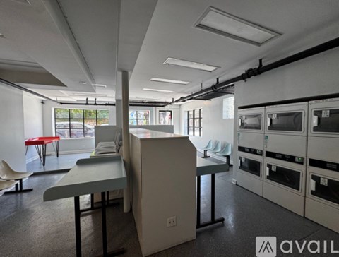 A kitchen area with a table and chairs in the foreground and a row of ovens in the background.