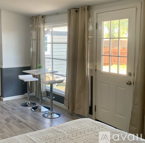 A white table and two stools are in front of a window with curtains.