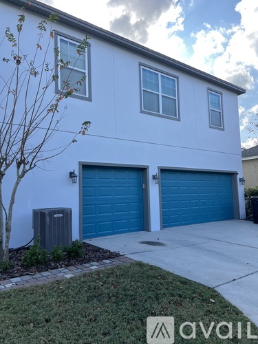 A white house with two blue garage doors and a tree in front.