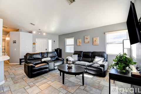 A living room with black leather couches and a stone floor.