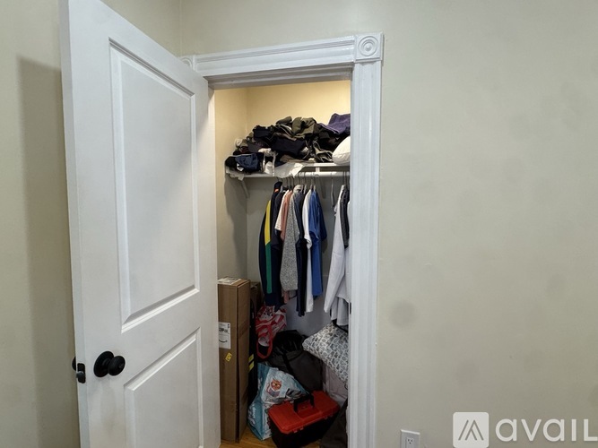 A white door opens to a small closet with clothes and shoes.