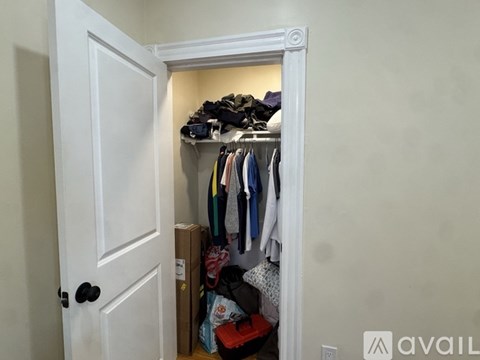 A white door opens to a small closet with clothes and shoes.