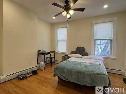 A bedroom with a bed, a desk, a chair, and a ceiling fan.
