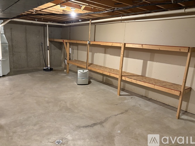 A spacious basement with concrete floors, wooden shelving, and exposed pipes.