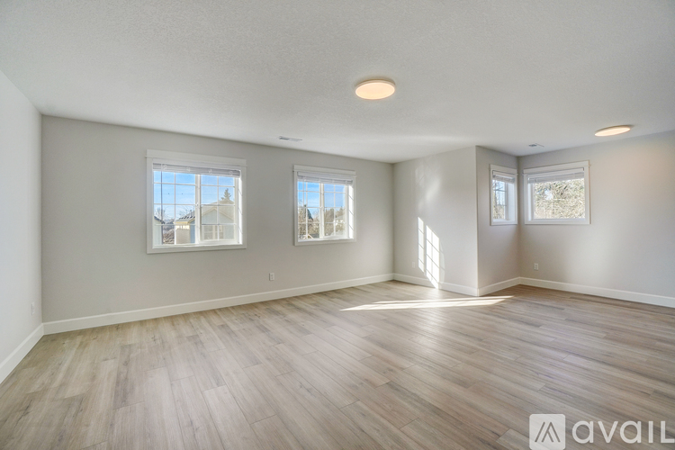 A spacious room with wooden flooring and three windows.
