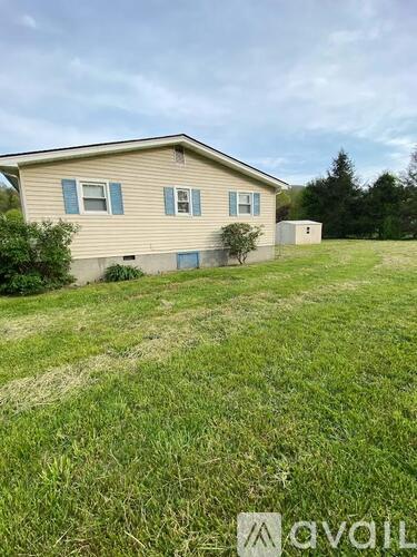 A beige house with a blue window is surrounded by a grassy field.