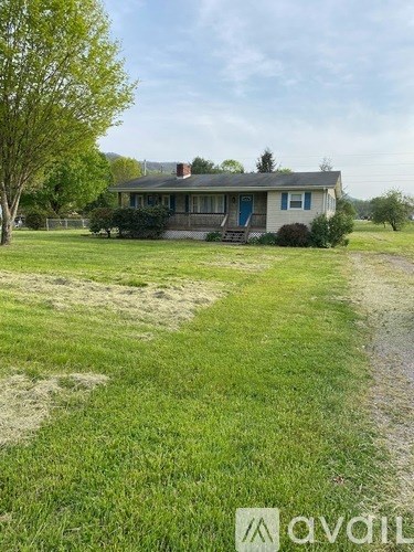 A beige house with a blue window is surrounded by a grassy field.