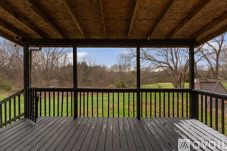 A wooden deck with a black railing and a view of a grassy field.