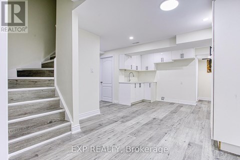 A white interior of a house with a staircase and a kitchen area.