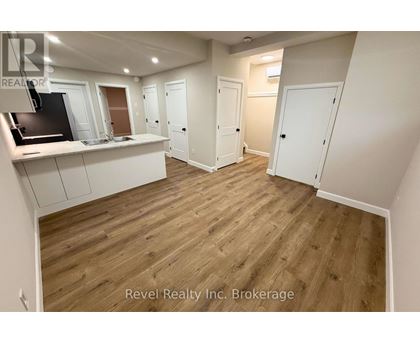 A room with wooden flooring and white walls, with a kitchen area on the left and a door on the right.