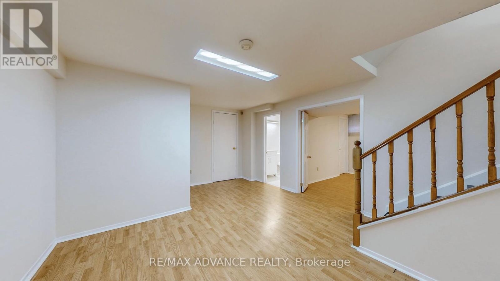 A spacious room with wooden flooring and white walls, featuring a staircase with wooden railings.