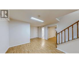 A spacious room with wooden flooring and white walls, featuring a staircase with wooden railings.