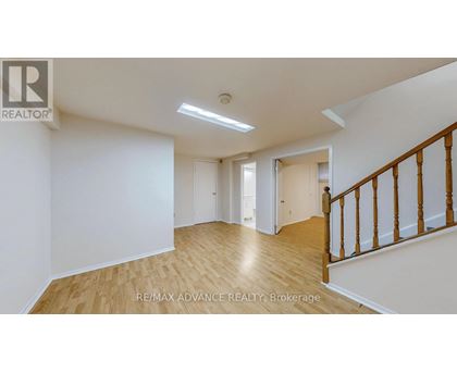 A spacious room with wooden flooring and white walls, featuring a staircase with wooden railings.